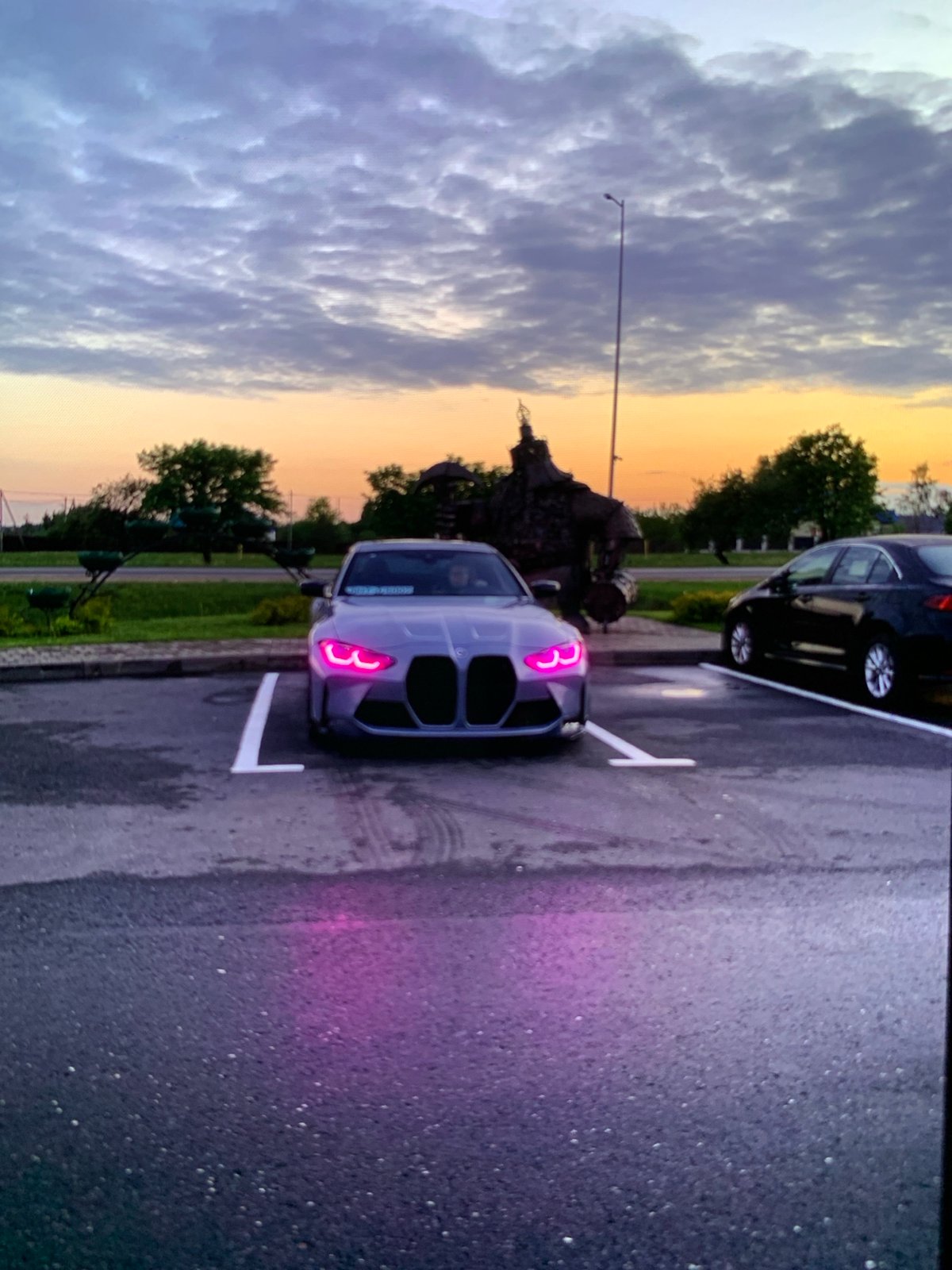 Gray BMW M3 parked at dusk with glowing pink headlights