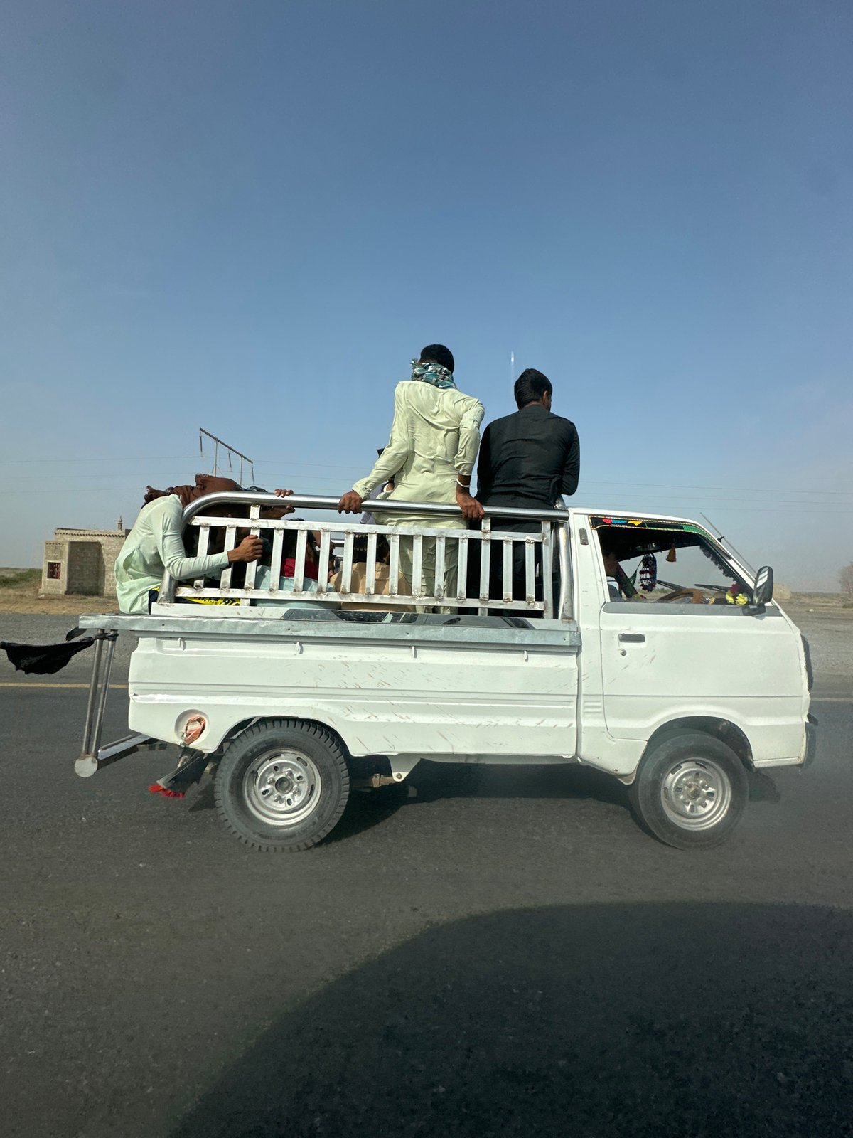 White pickup truck carrying passengers along a Pakistani road