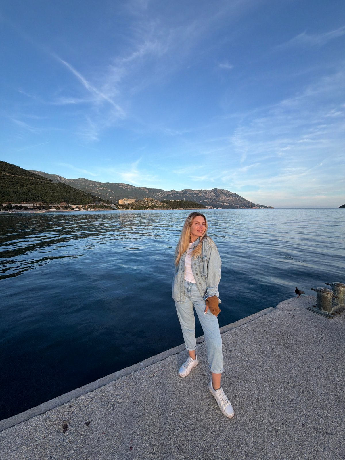 Woman with teddy bear sits on pier in Budva
