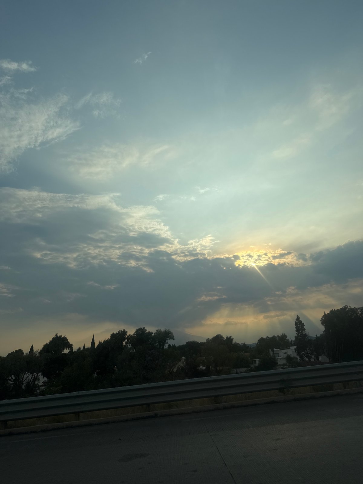 Cloudy skies with breaking sunlight observed over roadside area