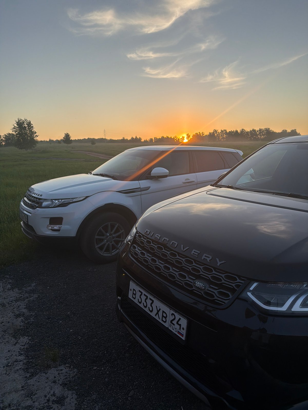 Two luxury SUVs parked in residential Krasnoyarsk during sunset