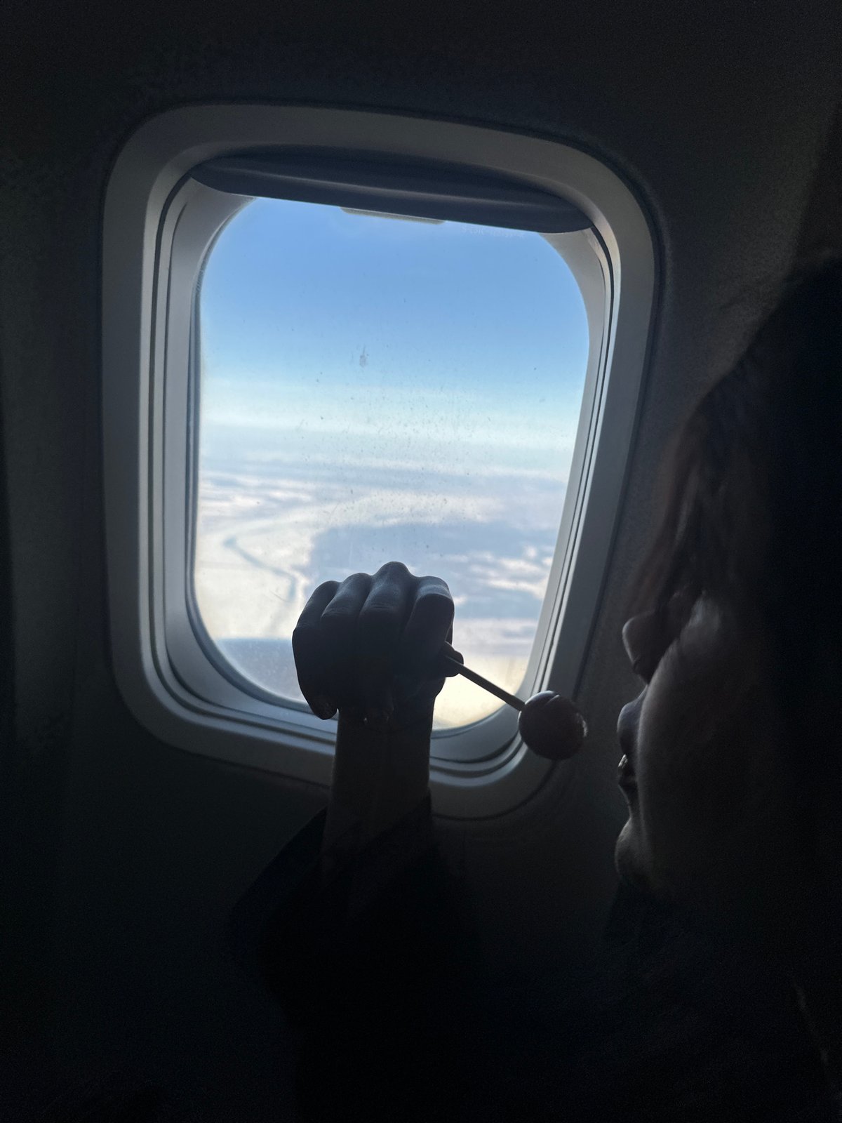 Airplane passenger enjoys lollipop while gazing out window