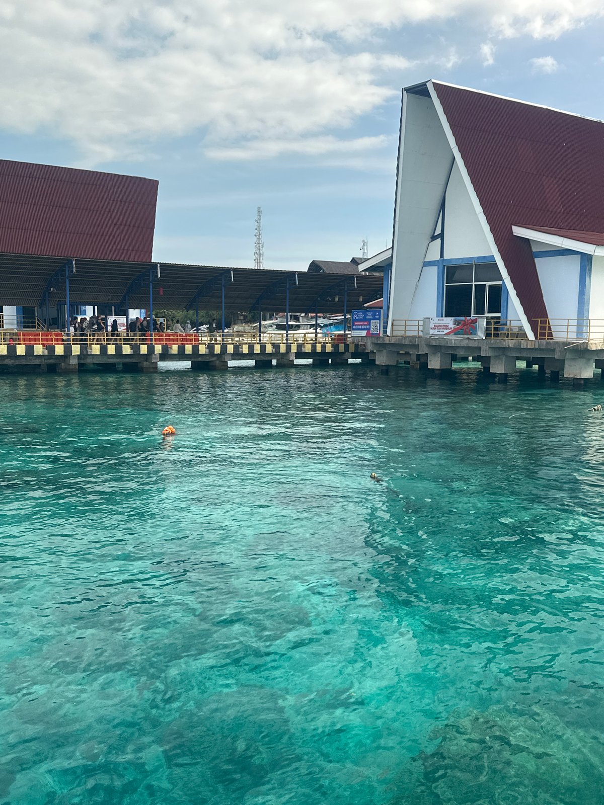 Boats navigate Indonesian waters near pier with mountainous backdrop