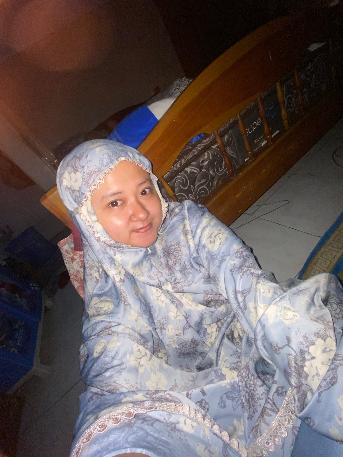 Woman in floral hijab rests on bed in Gelam