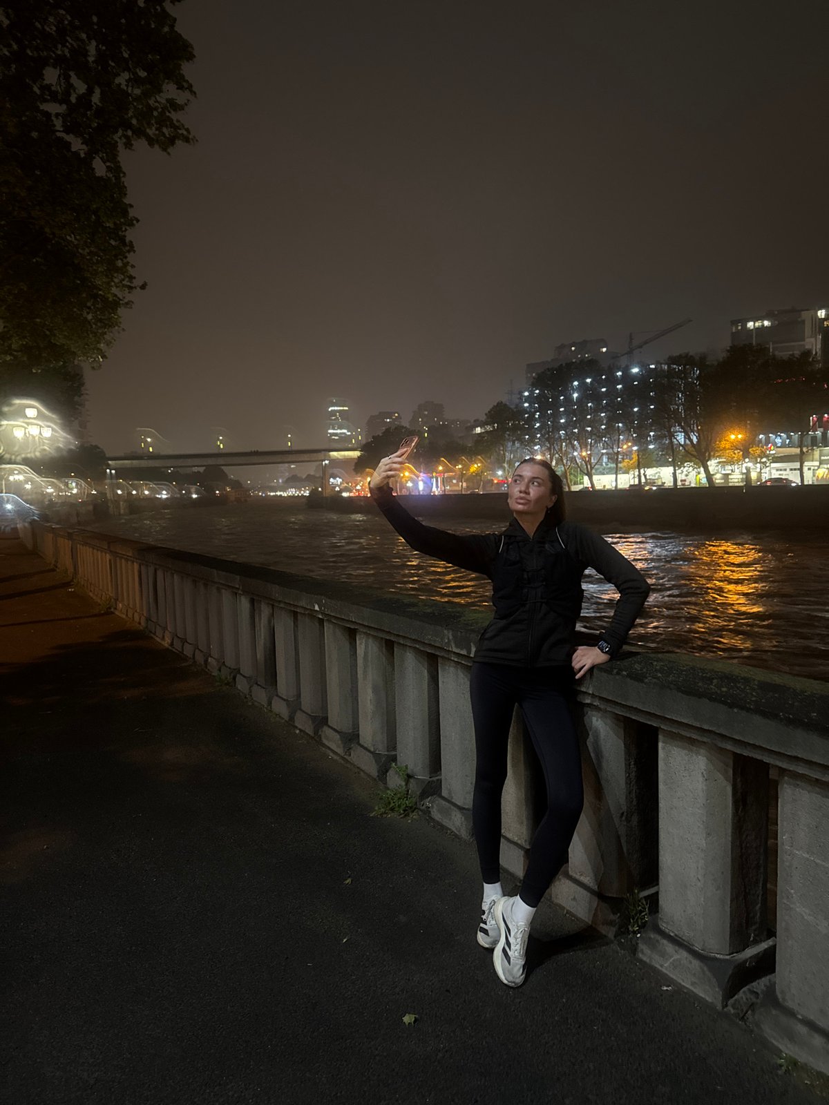 Woman poses with phone on riverside wall in Tbilisi