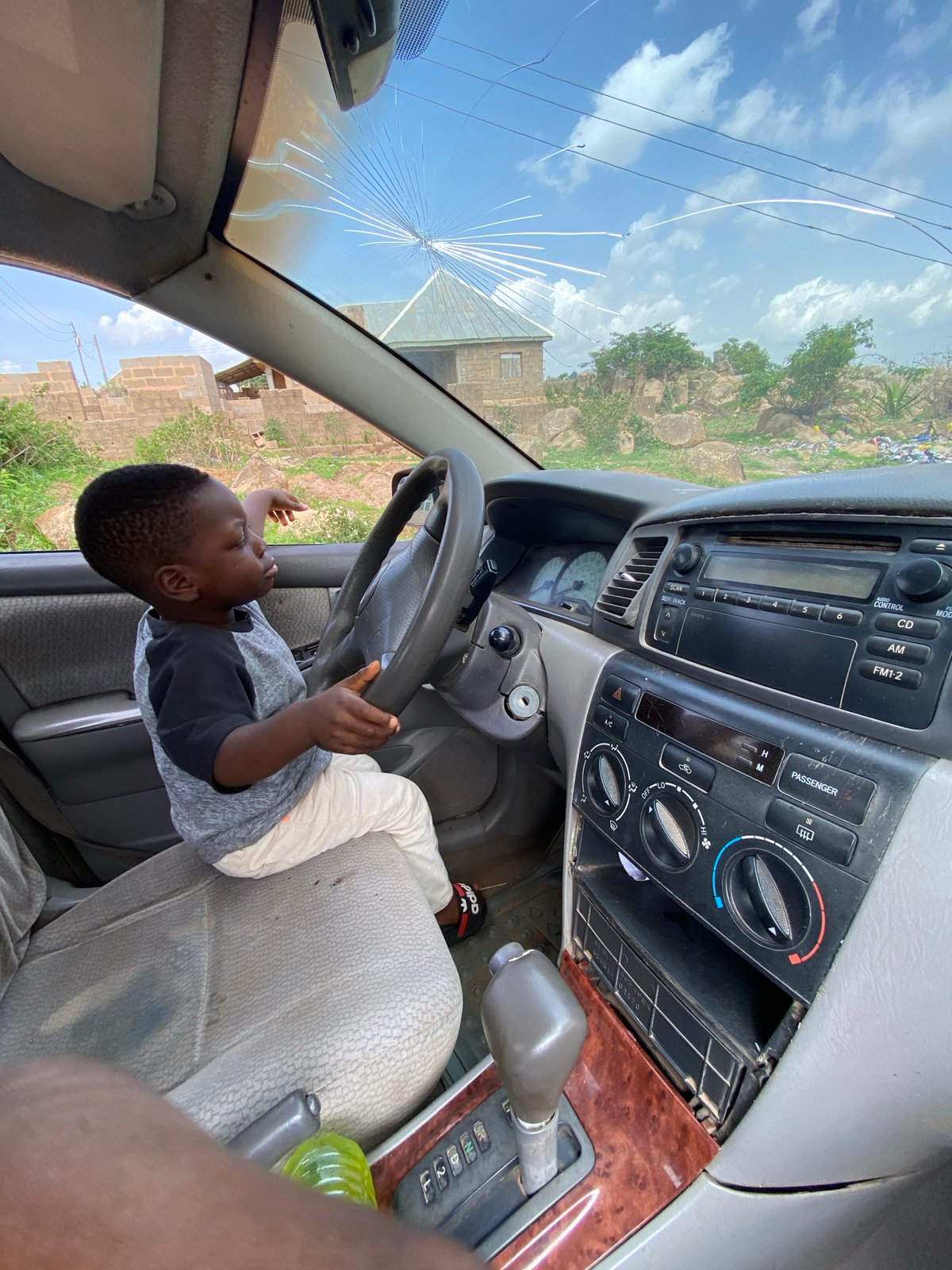 Child plays pretend driving game with parked car in Nigeria