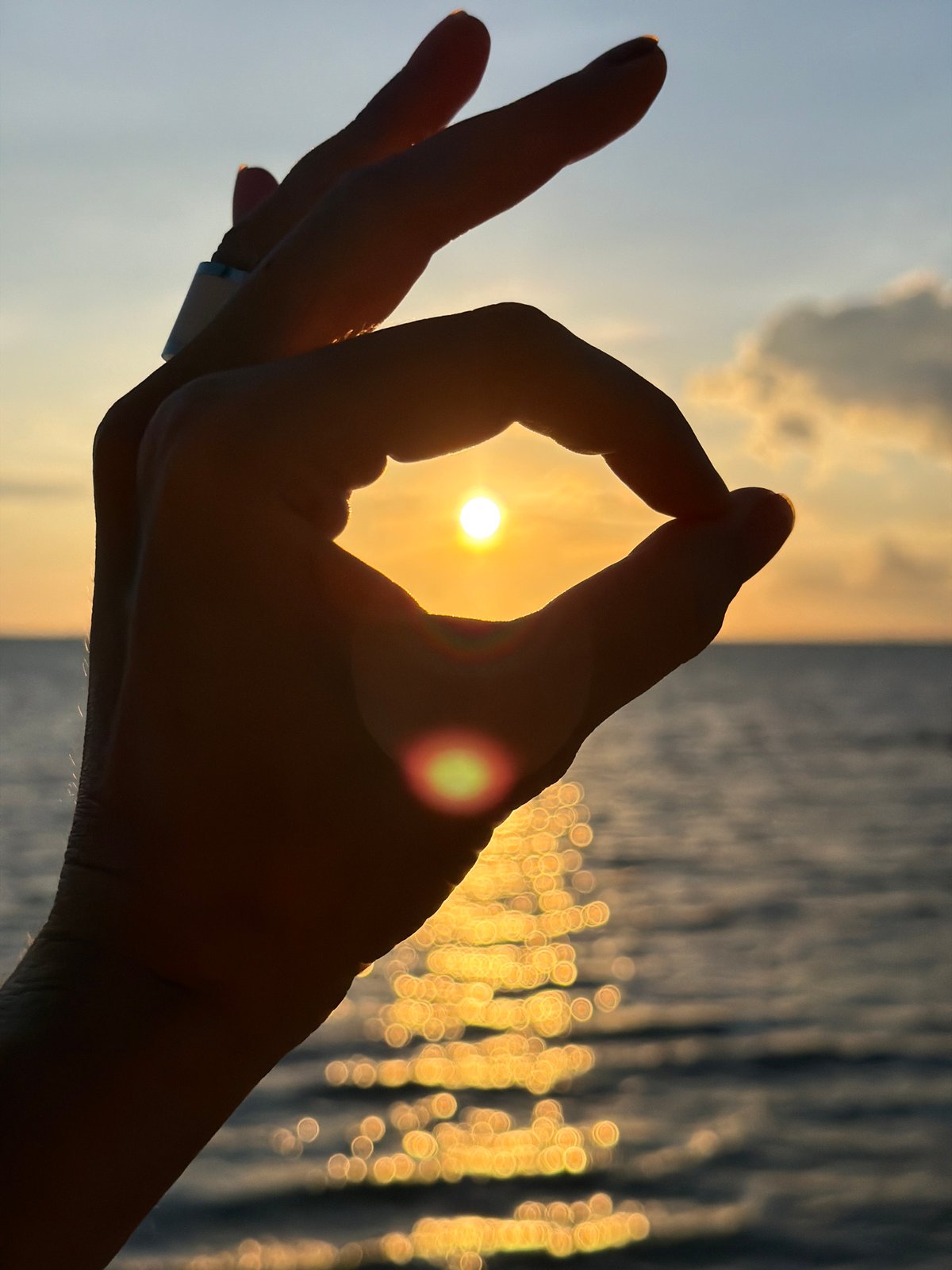 Golden sunset over Baan Plai Laem beach, hand framing the sun