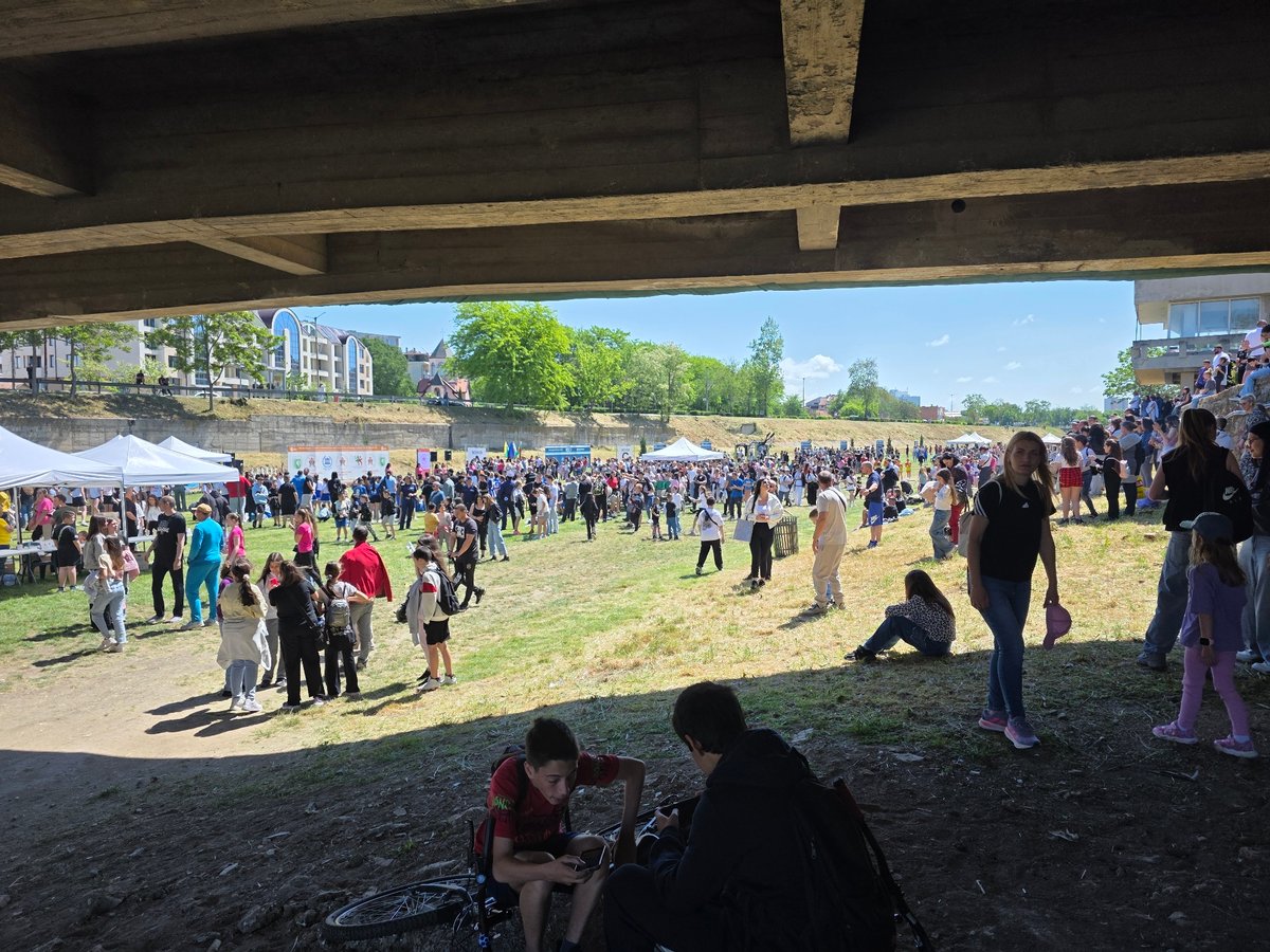 People gather in grassy area under concrete bridge