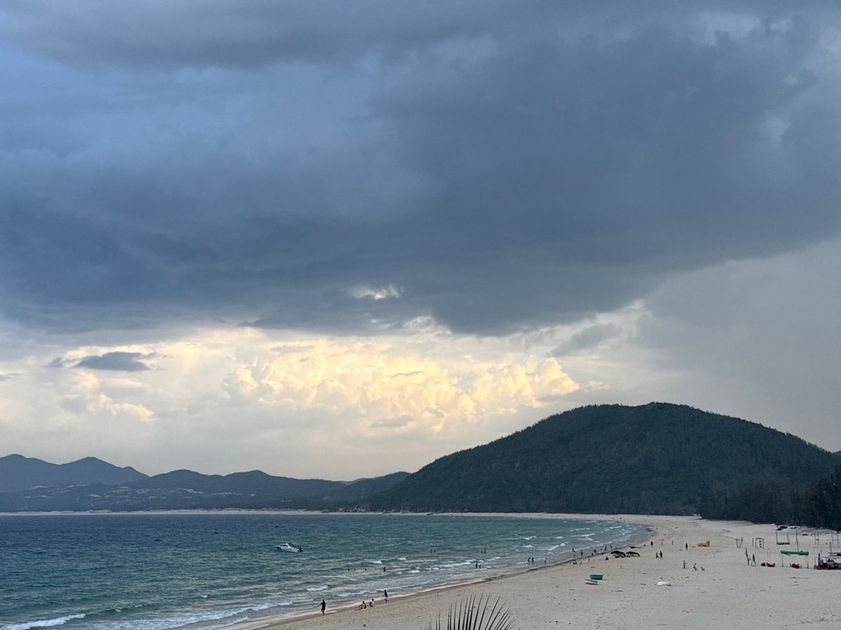 Stormy skies over a turquoise beach with scattered visitors