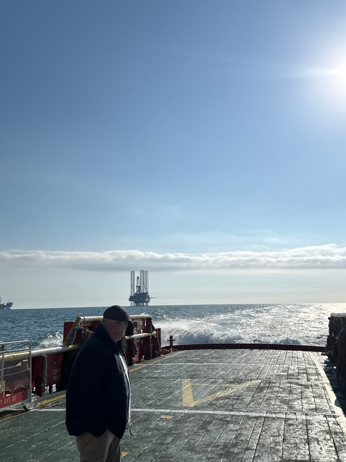 Man observes oil rig from ship deck in Italian waters