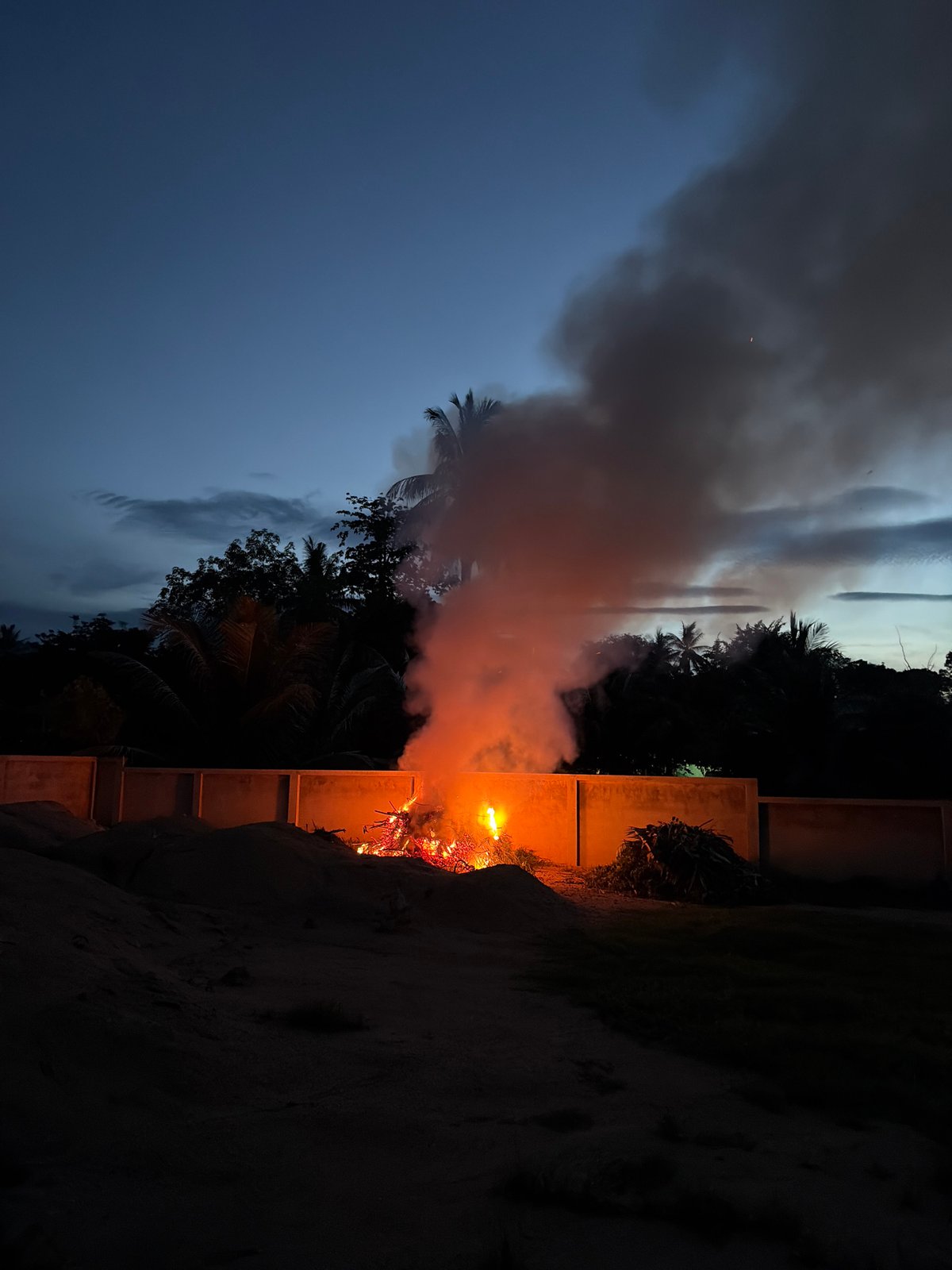 Bonfire burns at dusk under a crescent moon in Baan Mae Nam