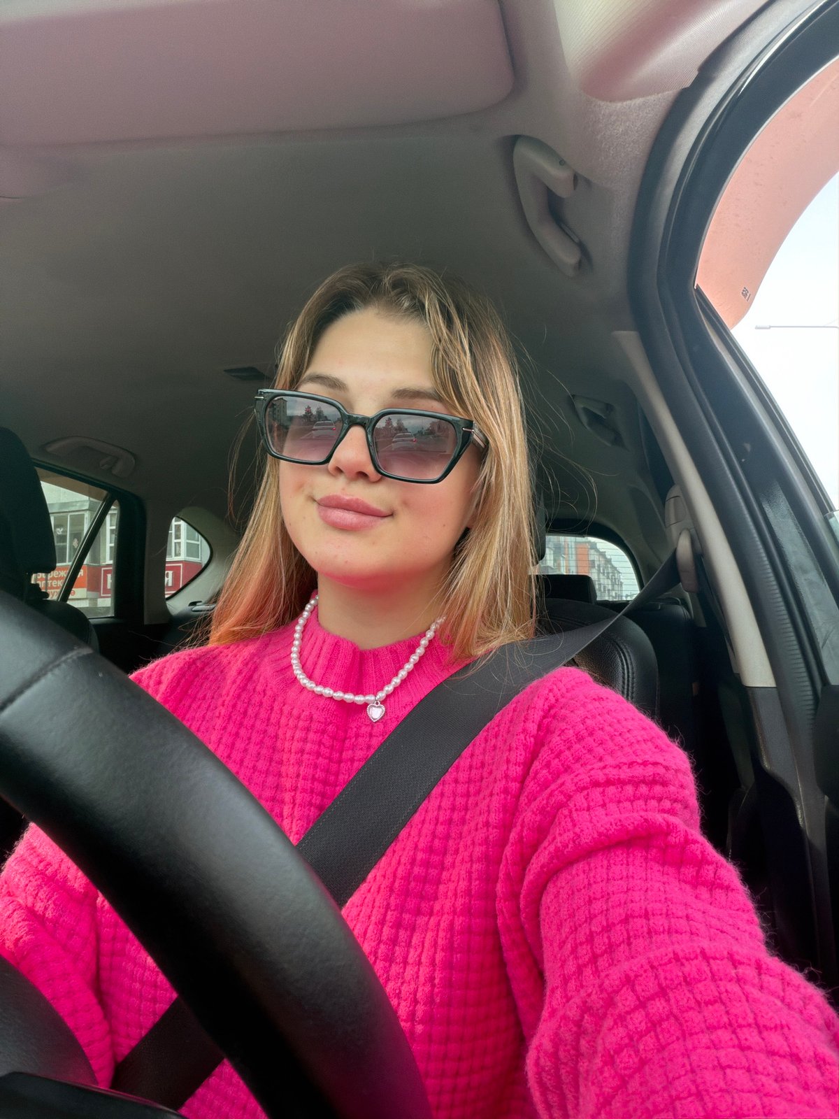 Woman in pink sweater poses playfully in car in Agryz