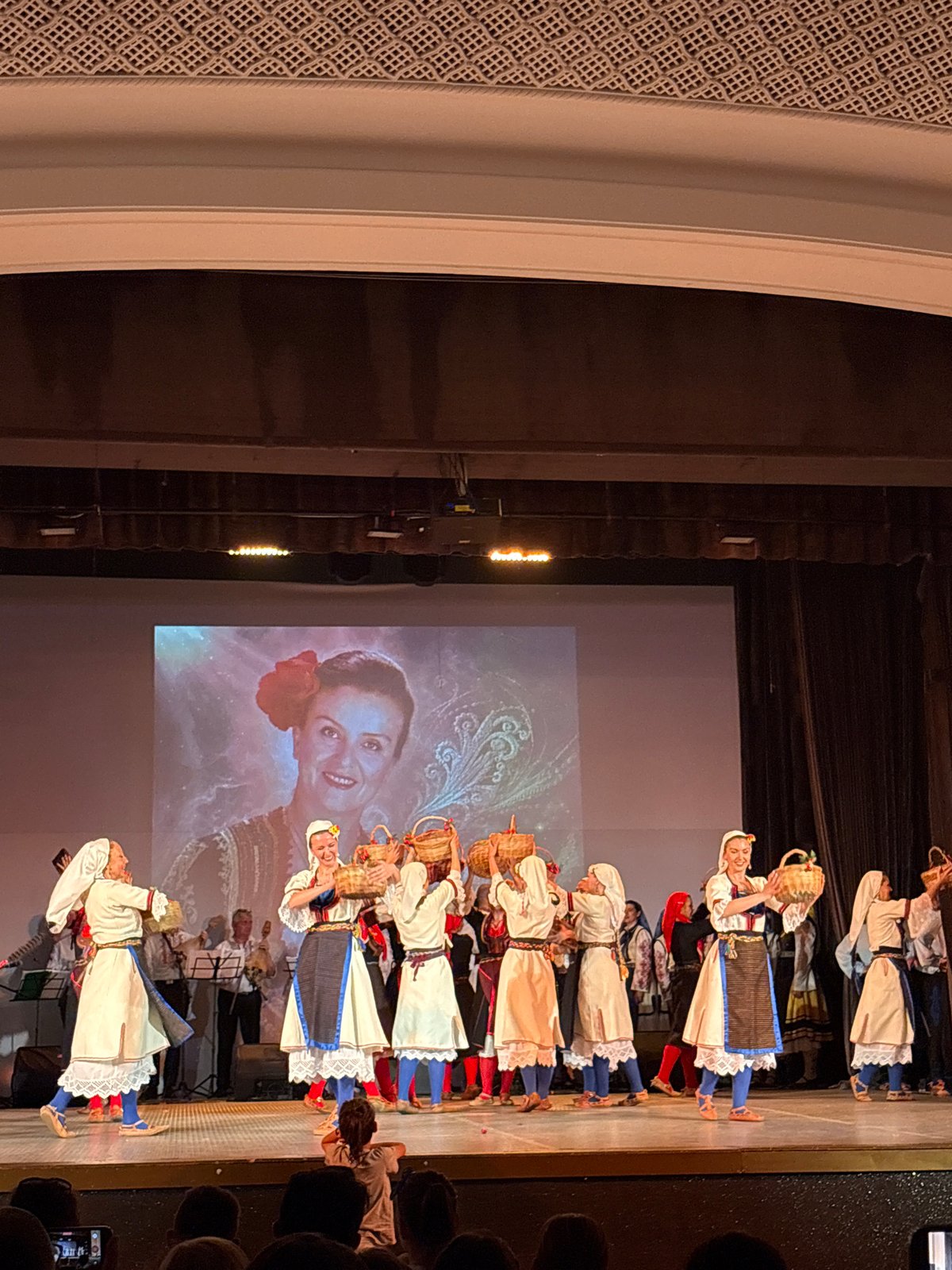 Traditional folk dance showcase on stage with projected backdrop
