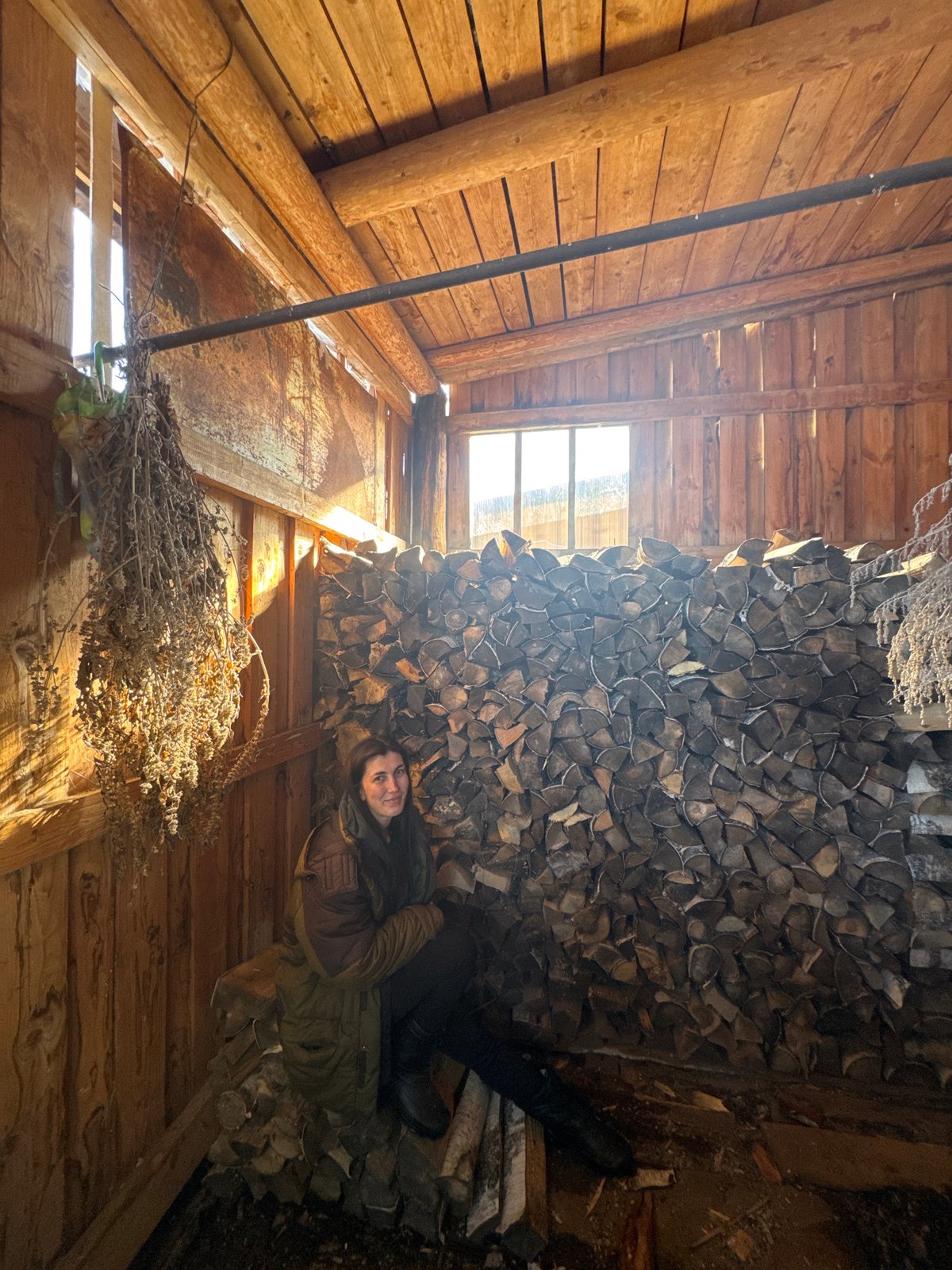 Woman rests on firewood pile in Russian wooden structure