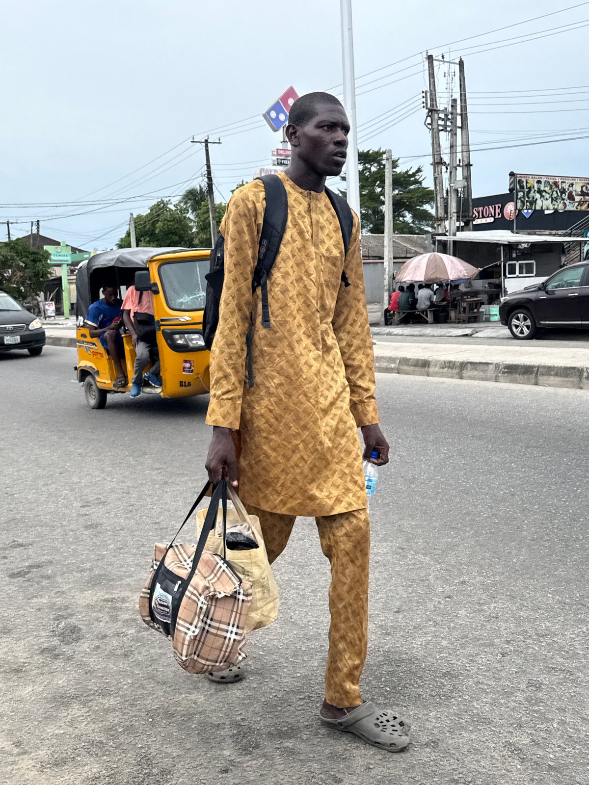 Man walks roadside carrying bag, water bottle in Ado