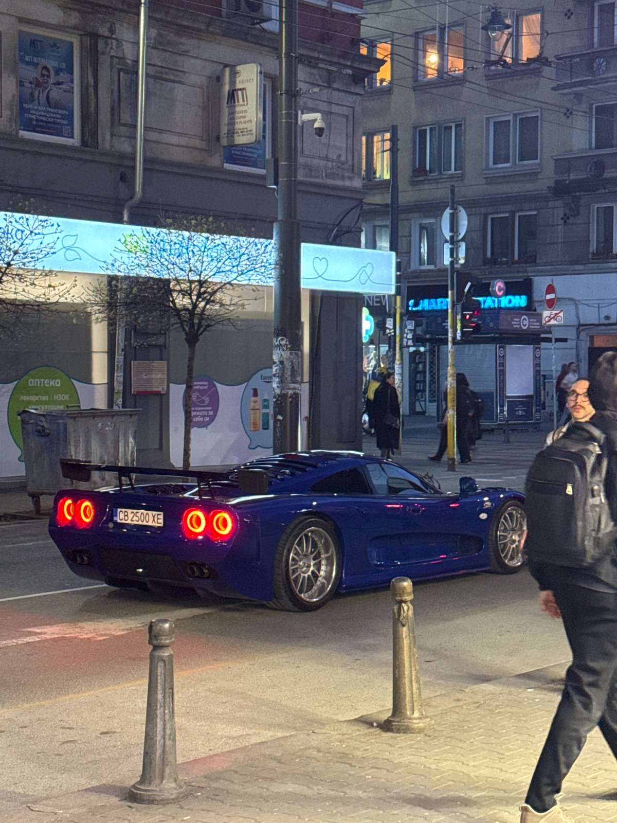 Blue sports car parks on Sofia sidewalk, person observed nearby