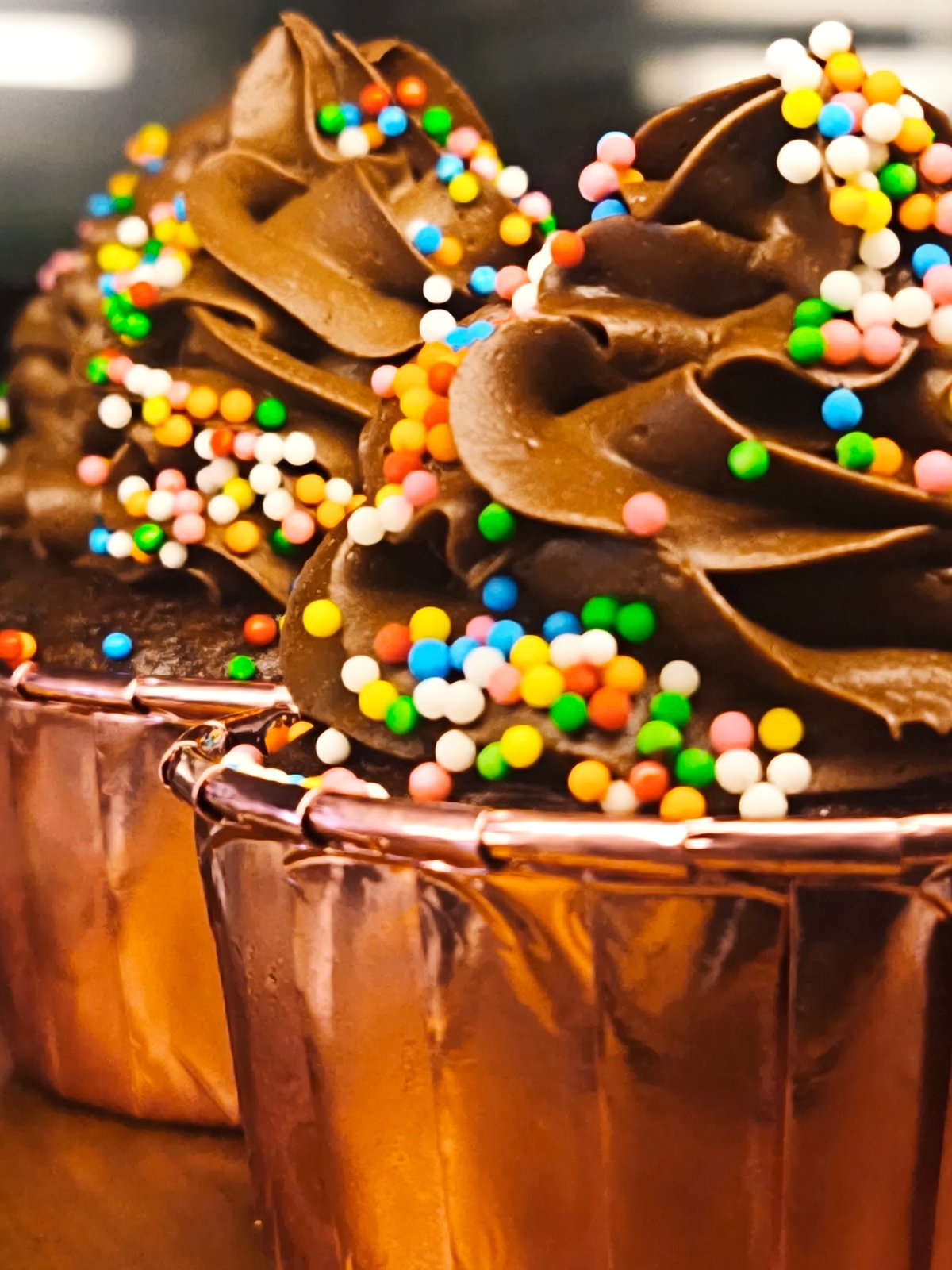 Chocolate cupcakes with rose-gold liners and colorful sprinkles