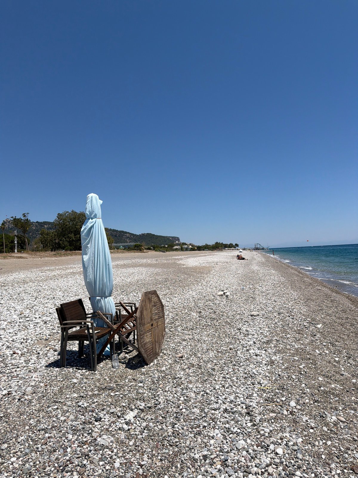 Busy pebble beach resort with water sports and a Neptune statue