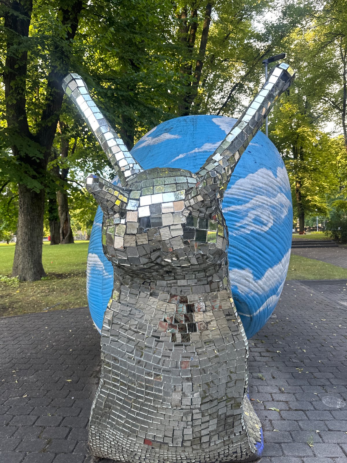 Riga park: mirrored snail sculpture and kayakers on a summer afternoon