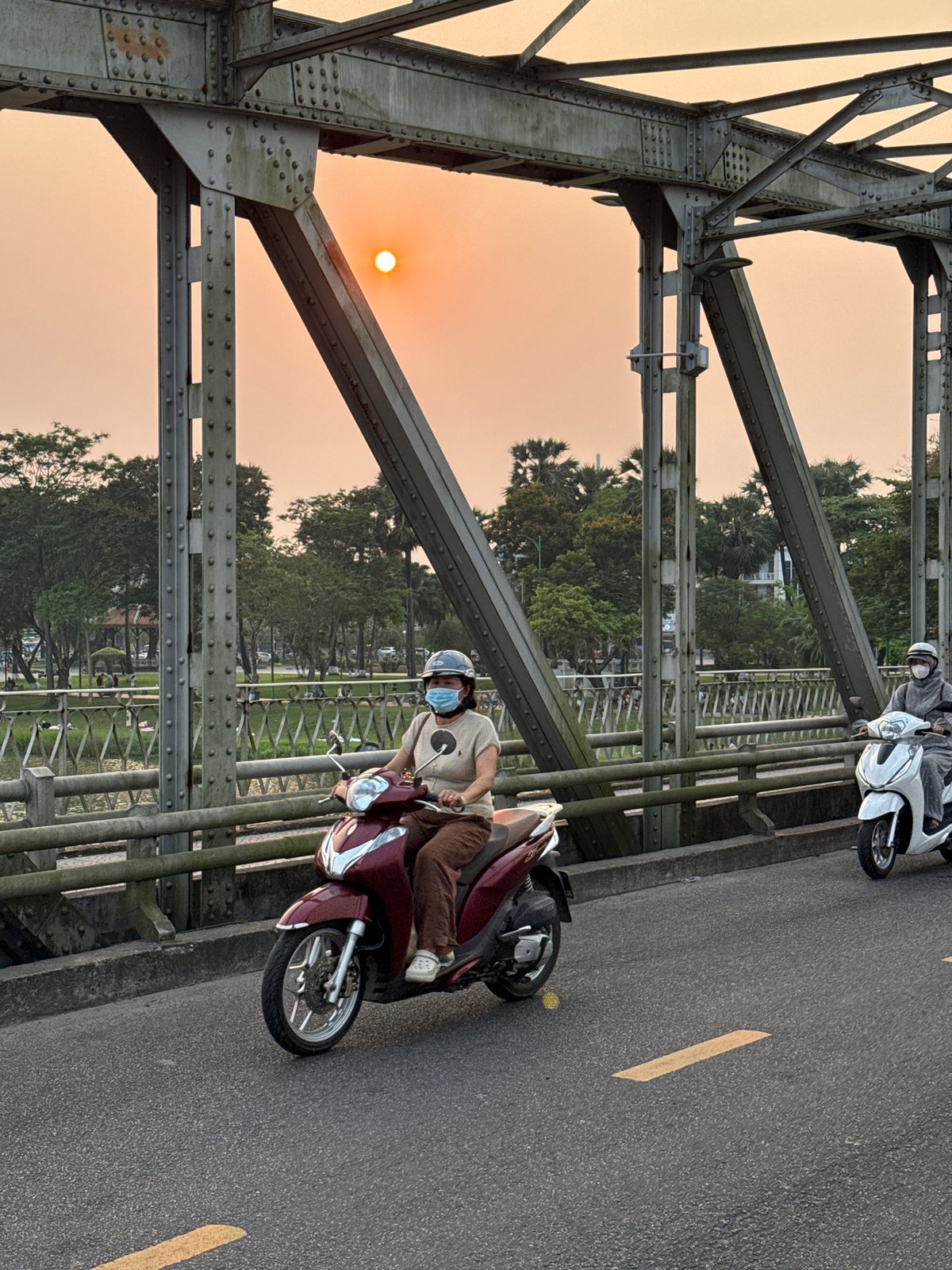 Motorbike riders cross bridge during sunset in Vietnam