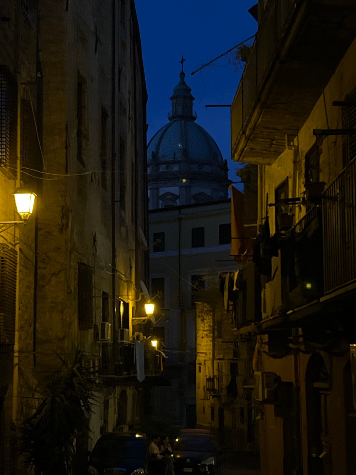 Domed church silhouette over a narrow Palermo street at dusk