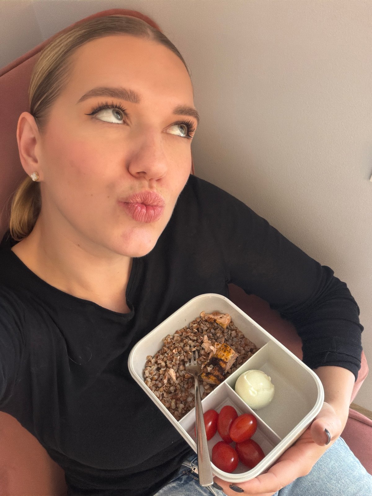 Woman eats compartmentalized lunch in pink chair, Riga