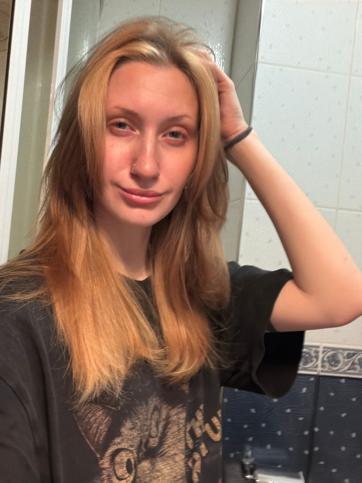 Bathroom mirror selfie session, black graphic tee, orange phone
