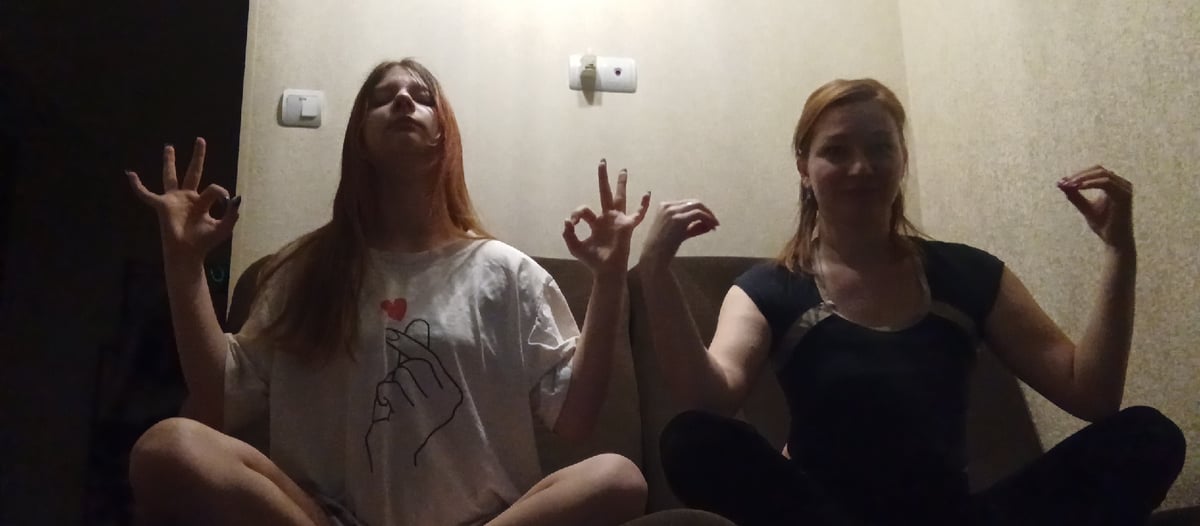 Two women sit together on brown couch indoors