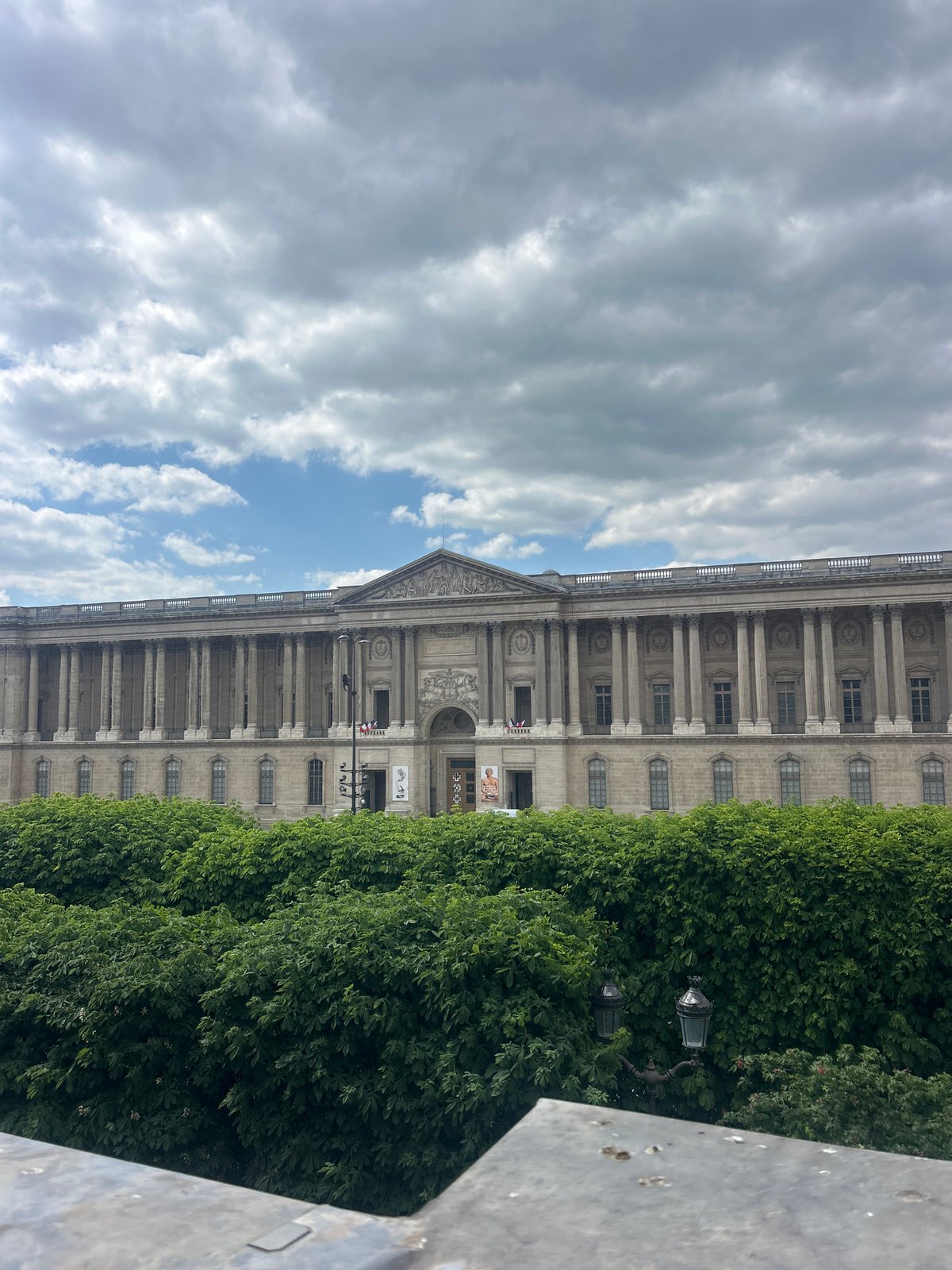 Classical building photographed amid green trees under cloudy sky