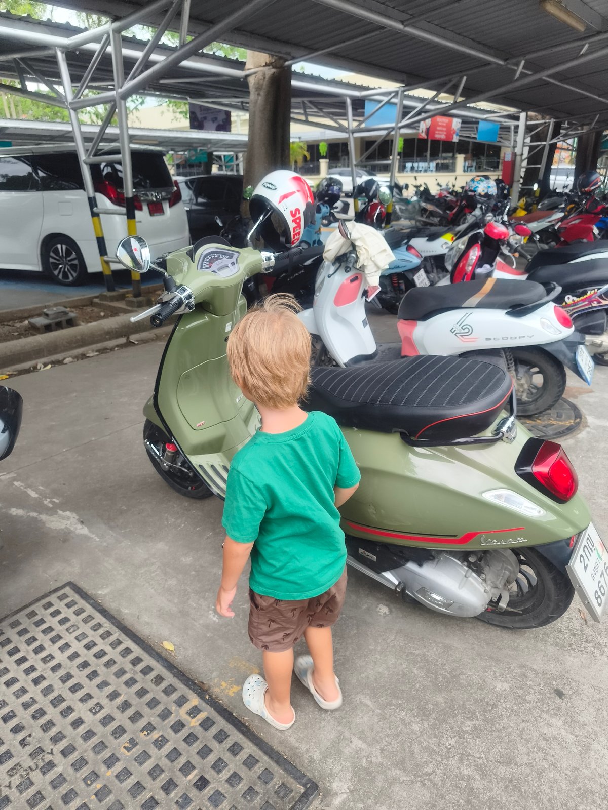 Child examines green scooter at Thai commercial complex