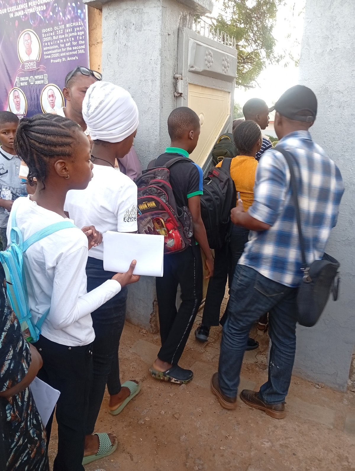 Students gather outside building with papers, backpacks