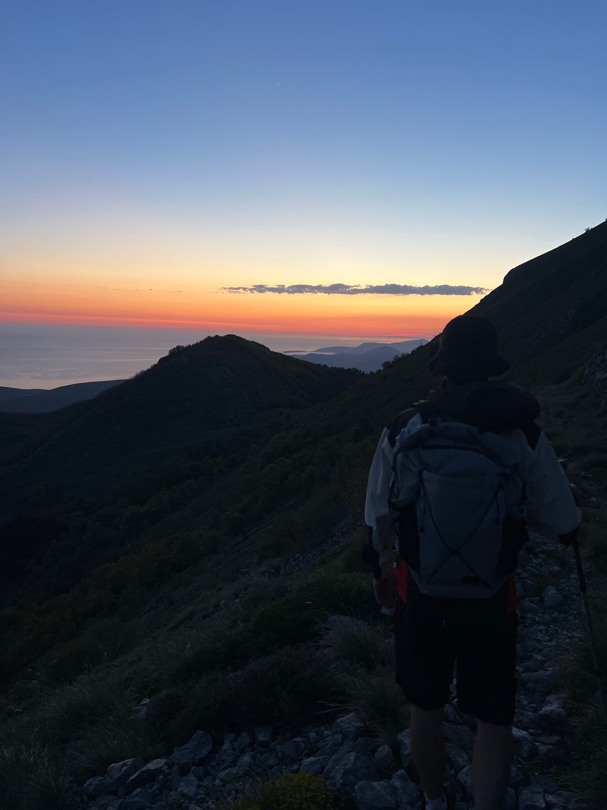 Hiker watches sunset from mountain slope in Dolovi, Montenegro