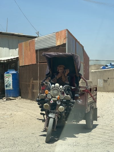 Three-wheeled vehicle travels Kandahar streets amid mountain backdrop