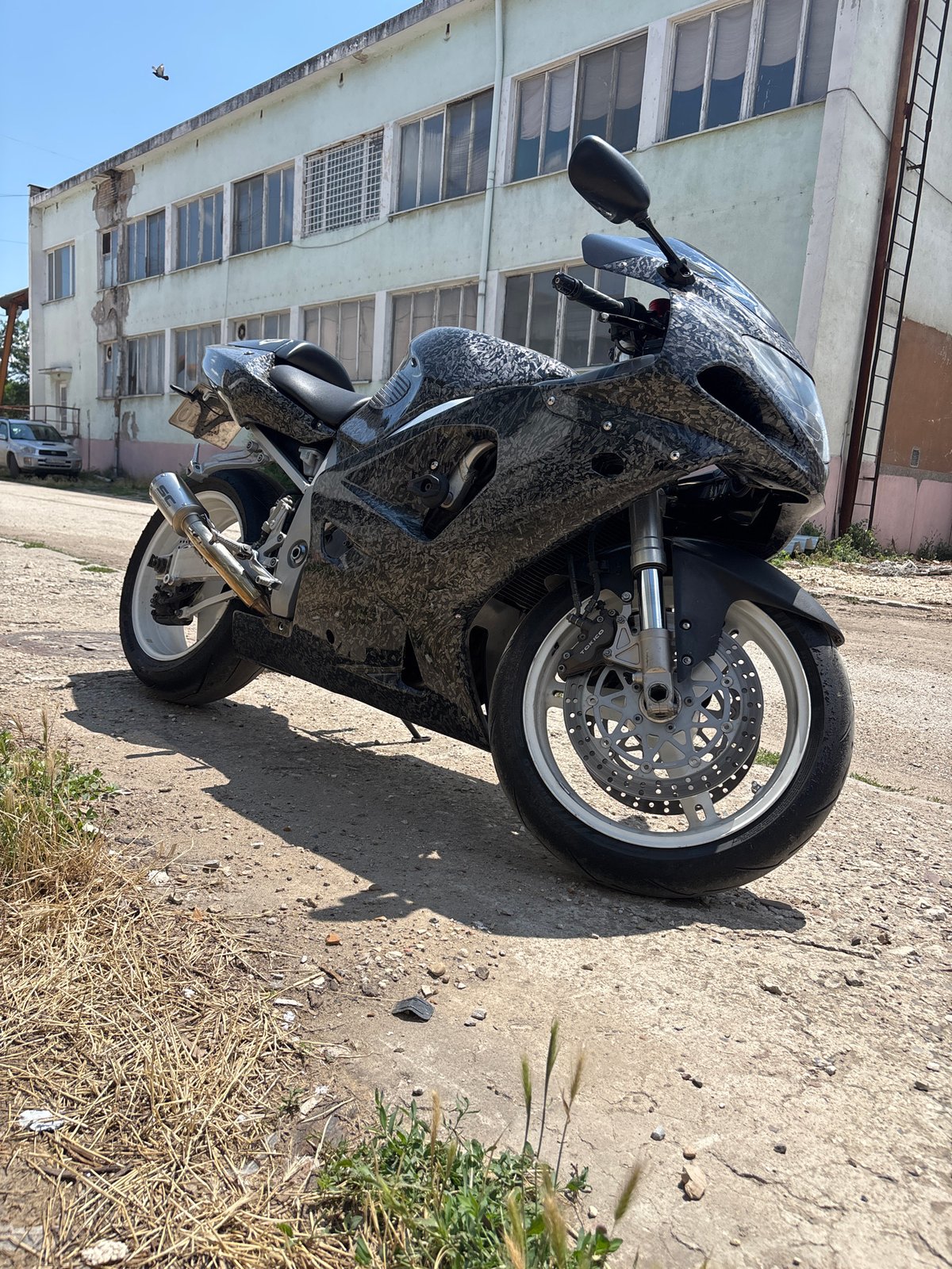 Camo sport bike parked outside weathered industrial building in Pleven
