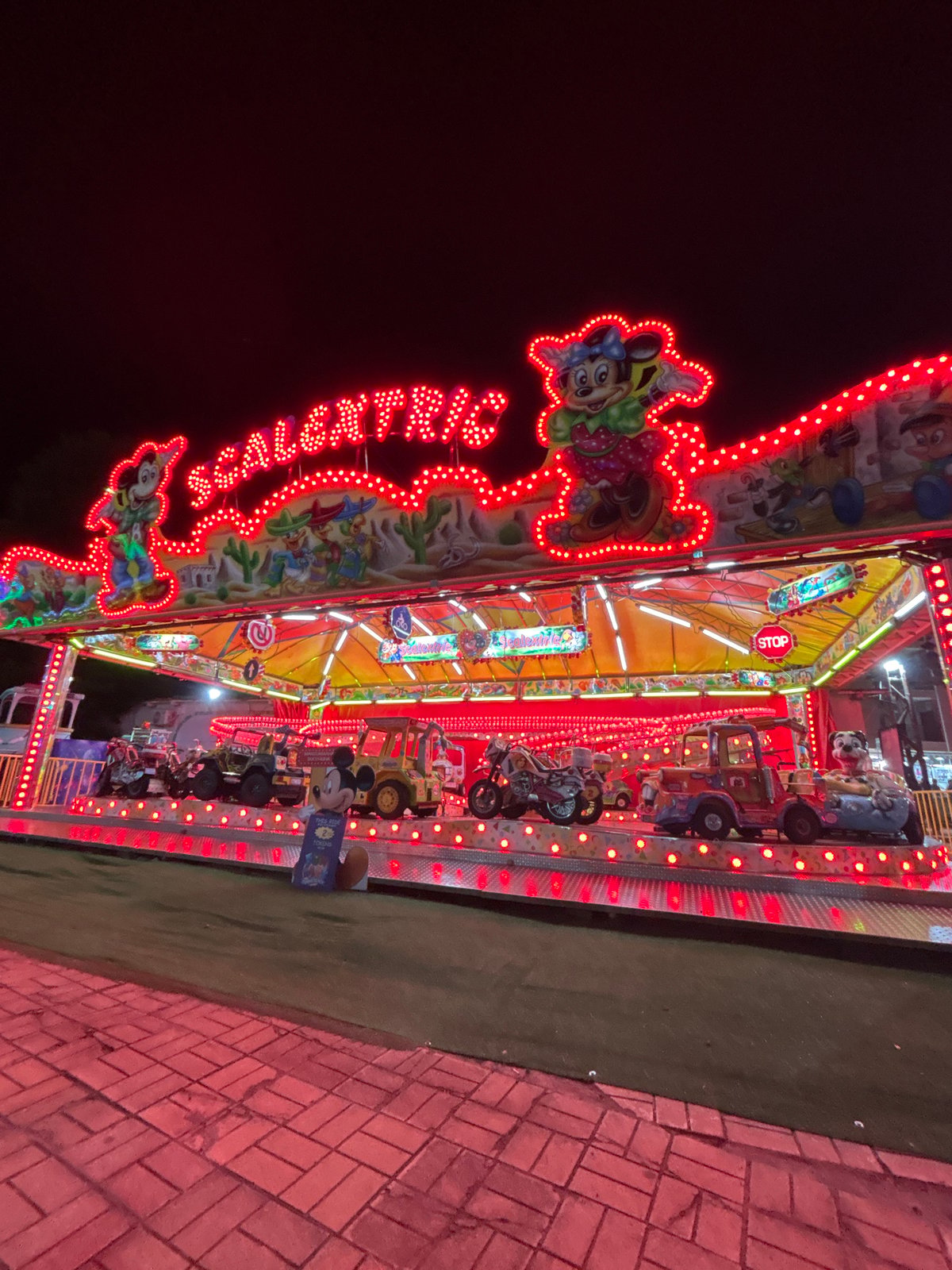 Evening at a Mickey Mouse-themed amusement park with multiple rides