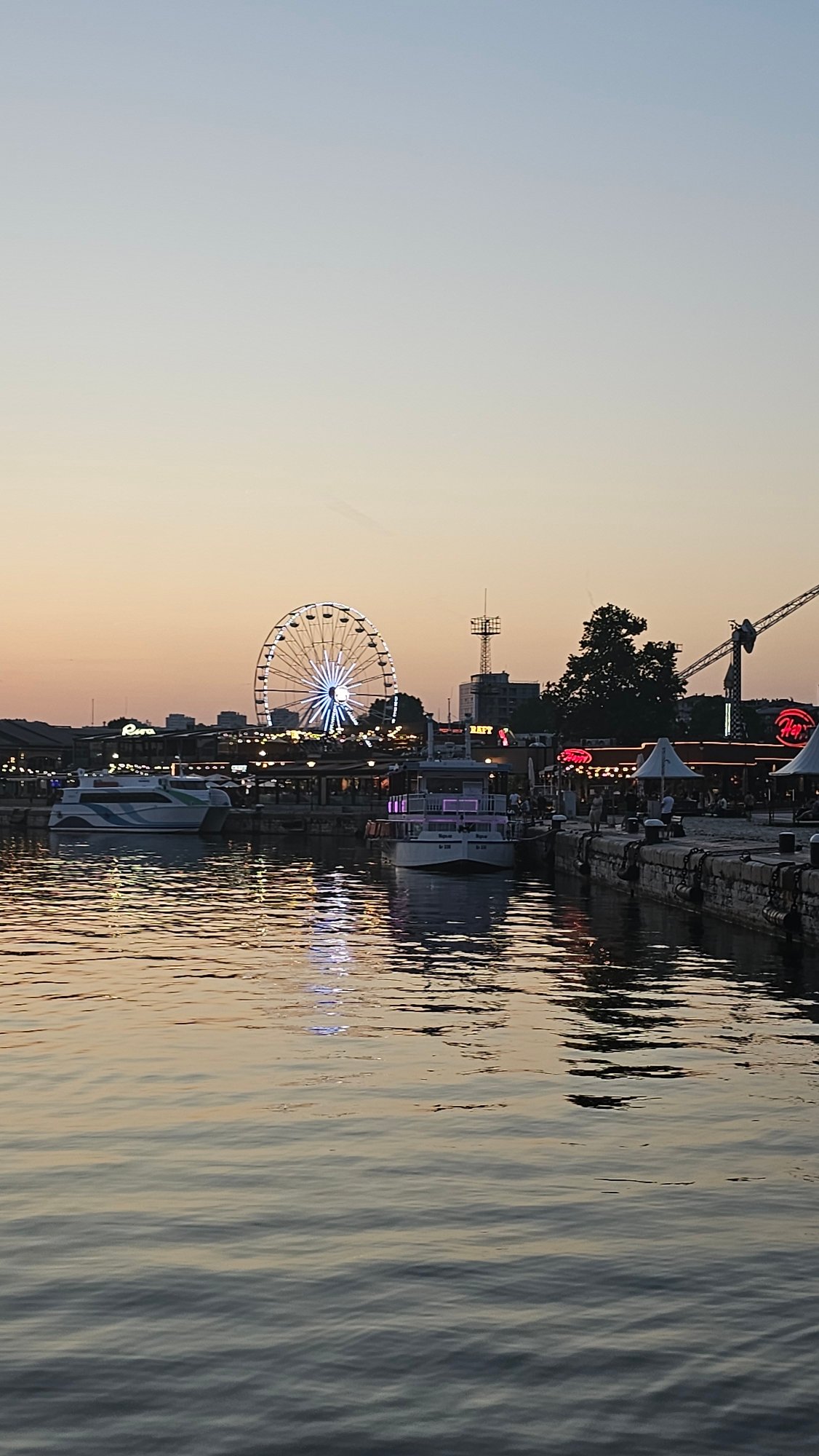 Varna harbor at dusk: Ferris wheel, sailboats, and a glowing sky