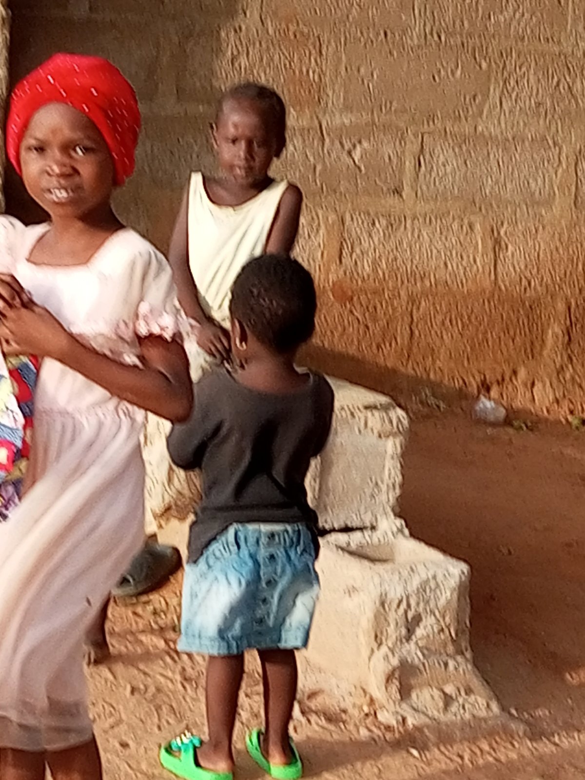 Children in a Nigerian courtyard beside an earthen wall