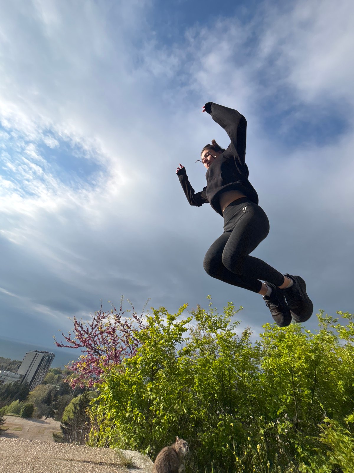 Woman performs athletic jumps, interacts with cat in urban setting