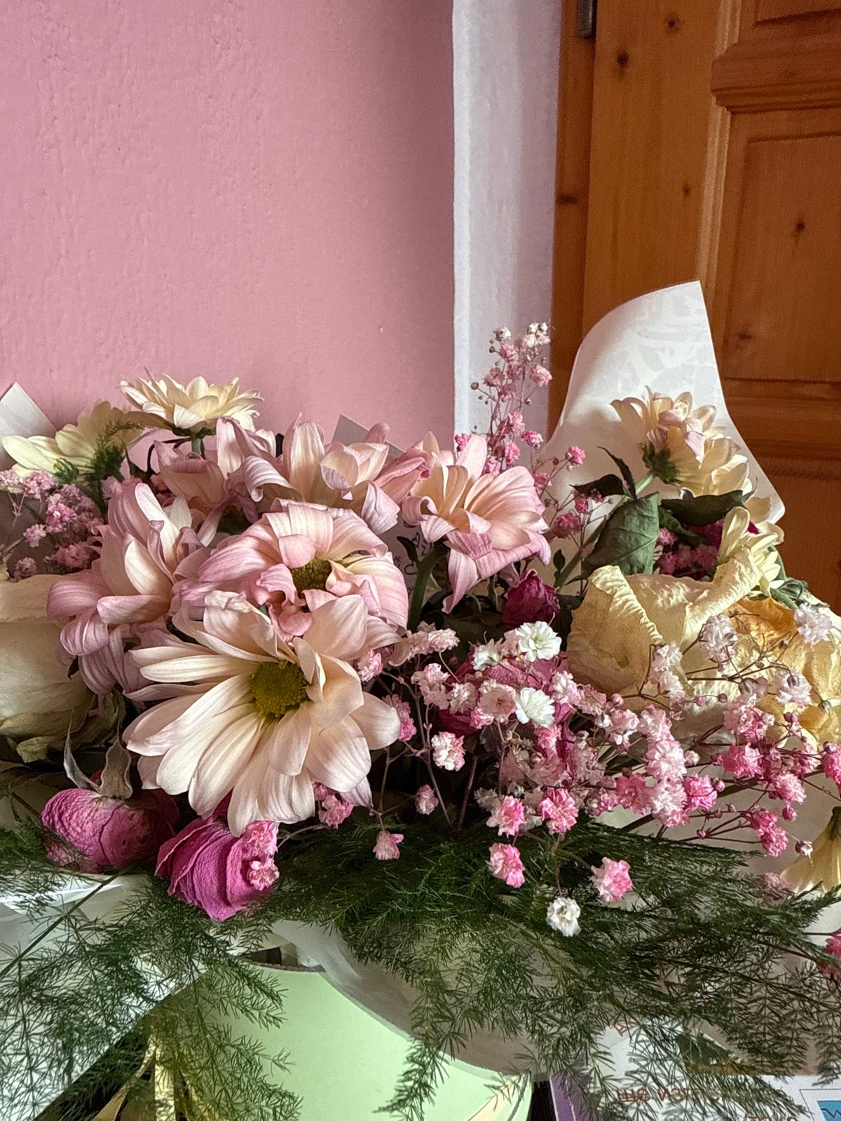 Dried flower bouquet documented against pink wall, wooden panel