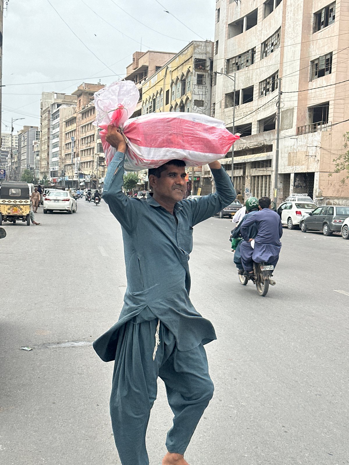 Carrying a large striped bag across a Karachi street