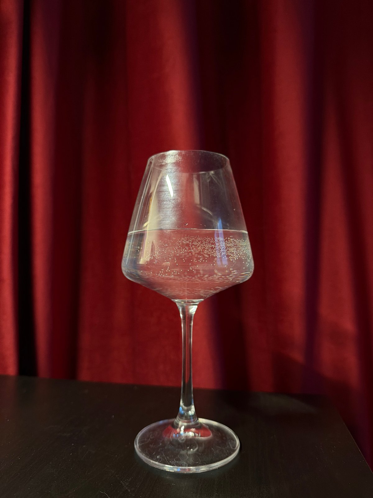 Wine glass with clear liquid observed on dark surface
