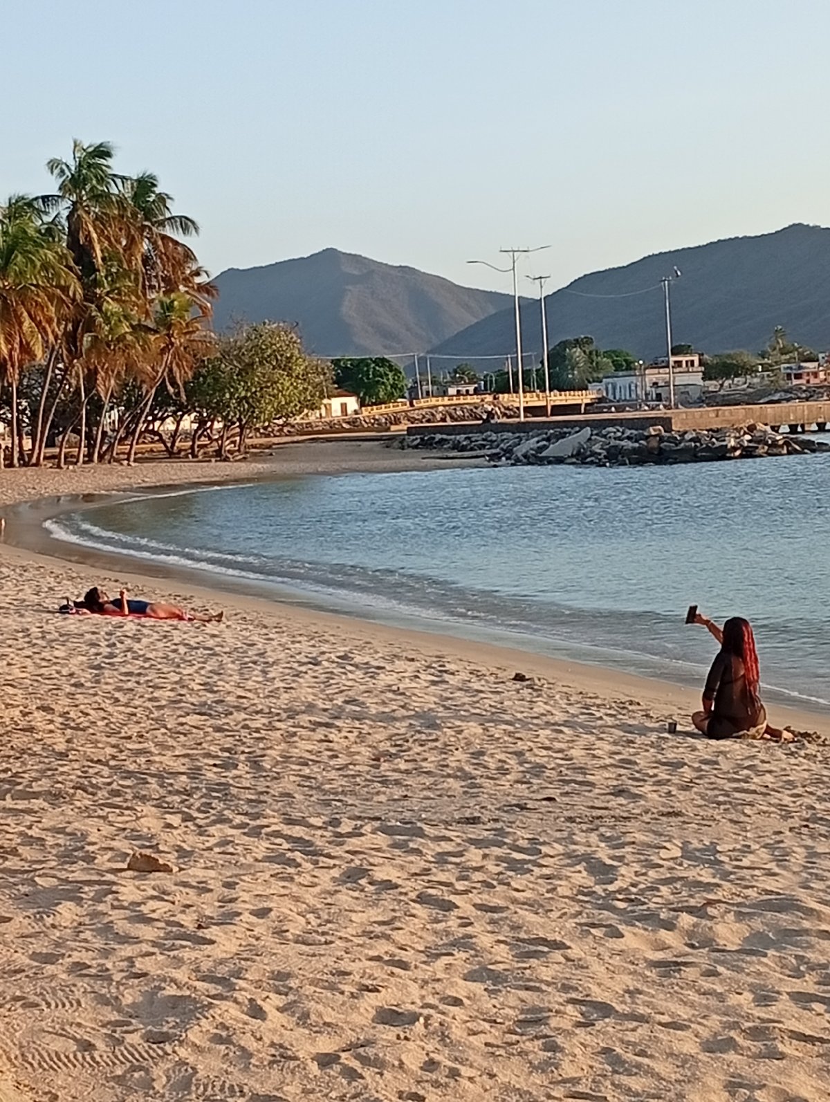 Woman documents sunset beach evening with boats and historic landmarks