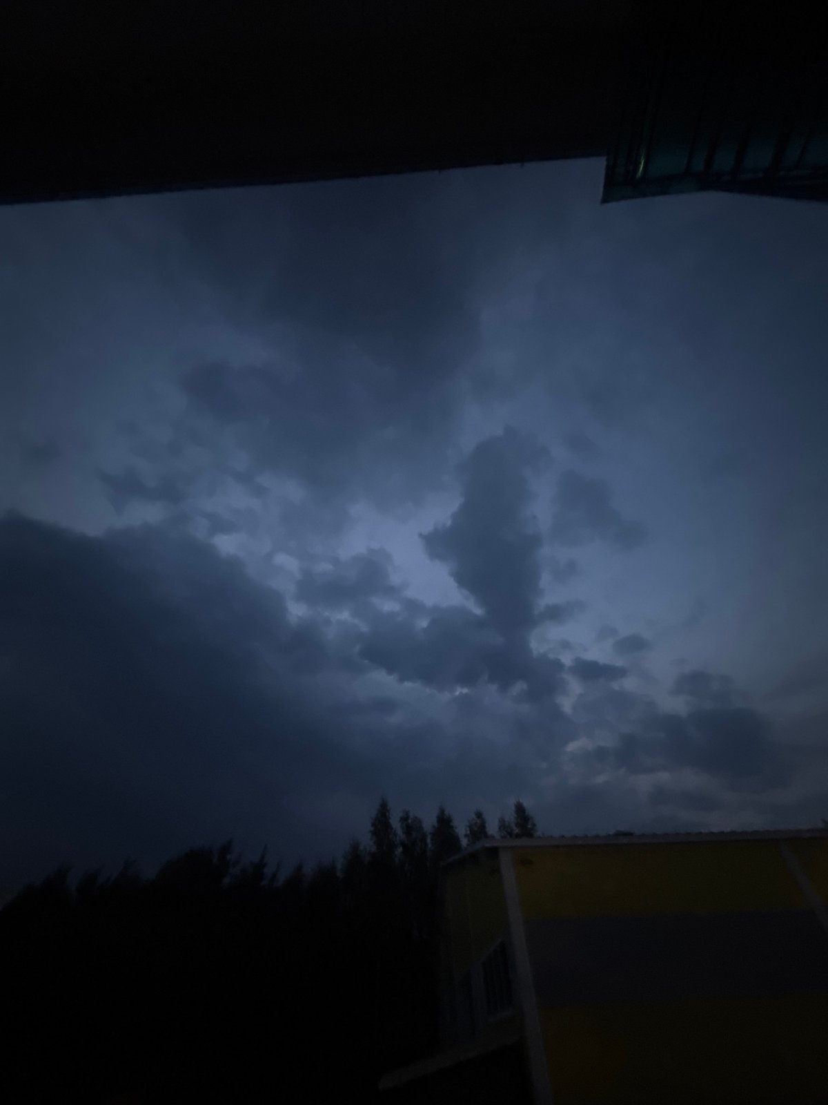 Storm clouds gather at dusk over urban rooftops and a cell tower