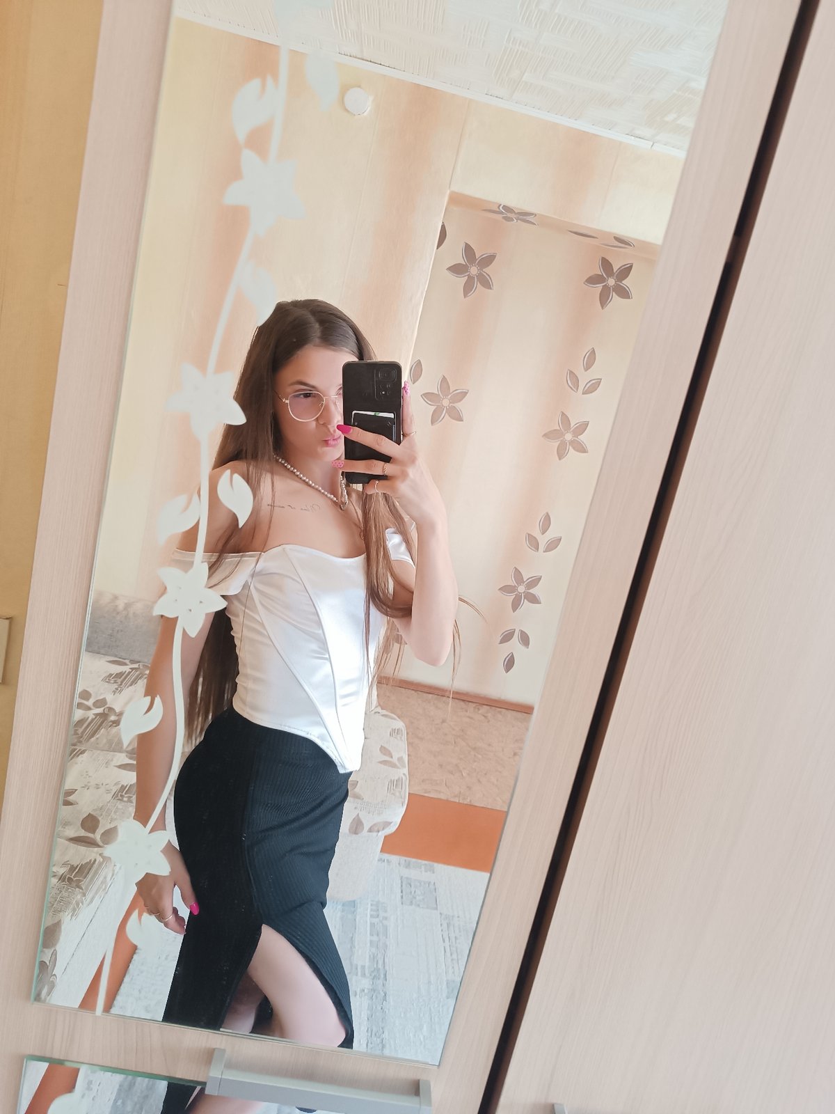 Woman takes mirror selfies in white top, black skirt