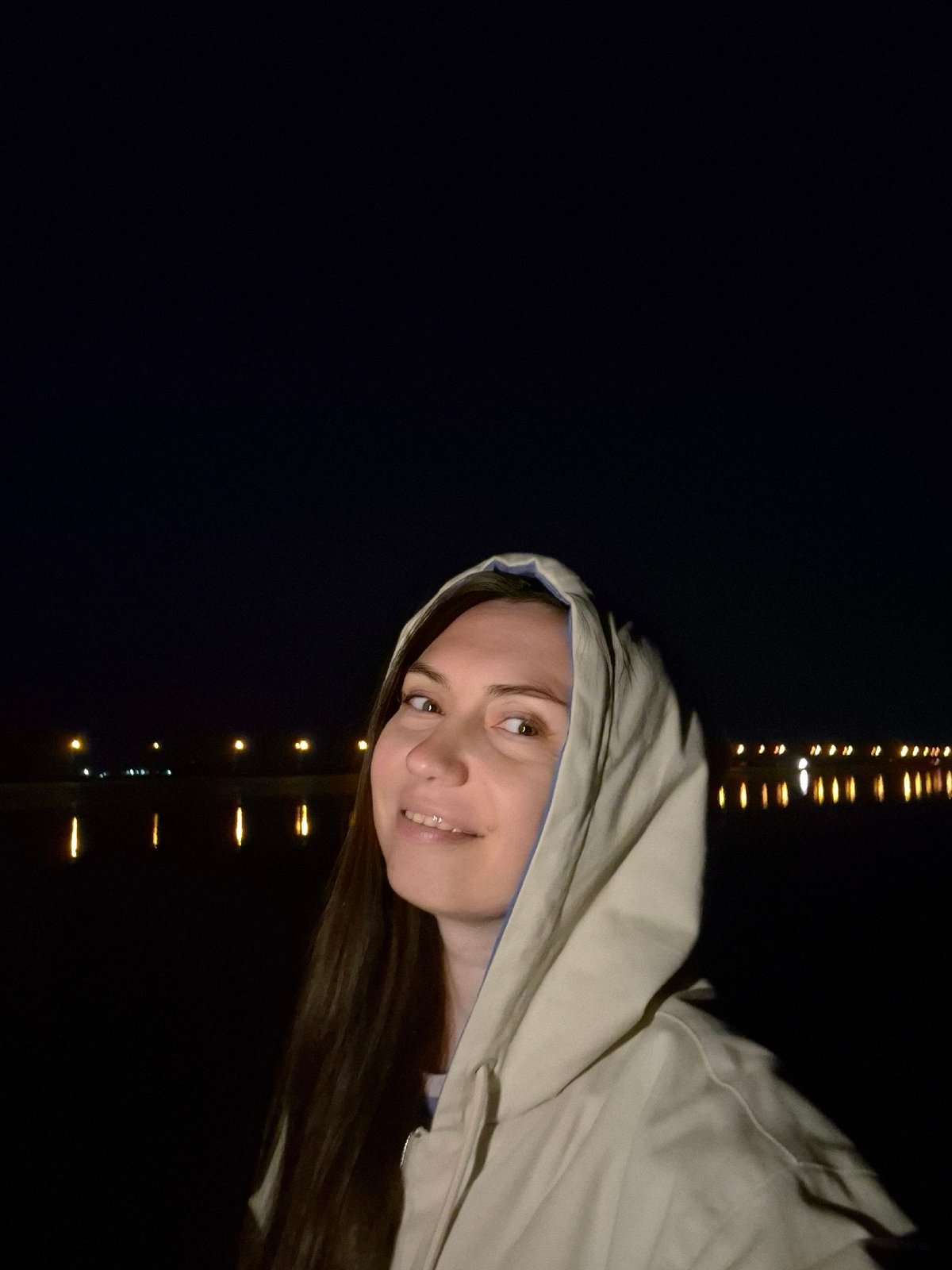 Woman in hooded jacket photographed smiling near yellow lights