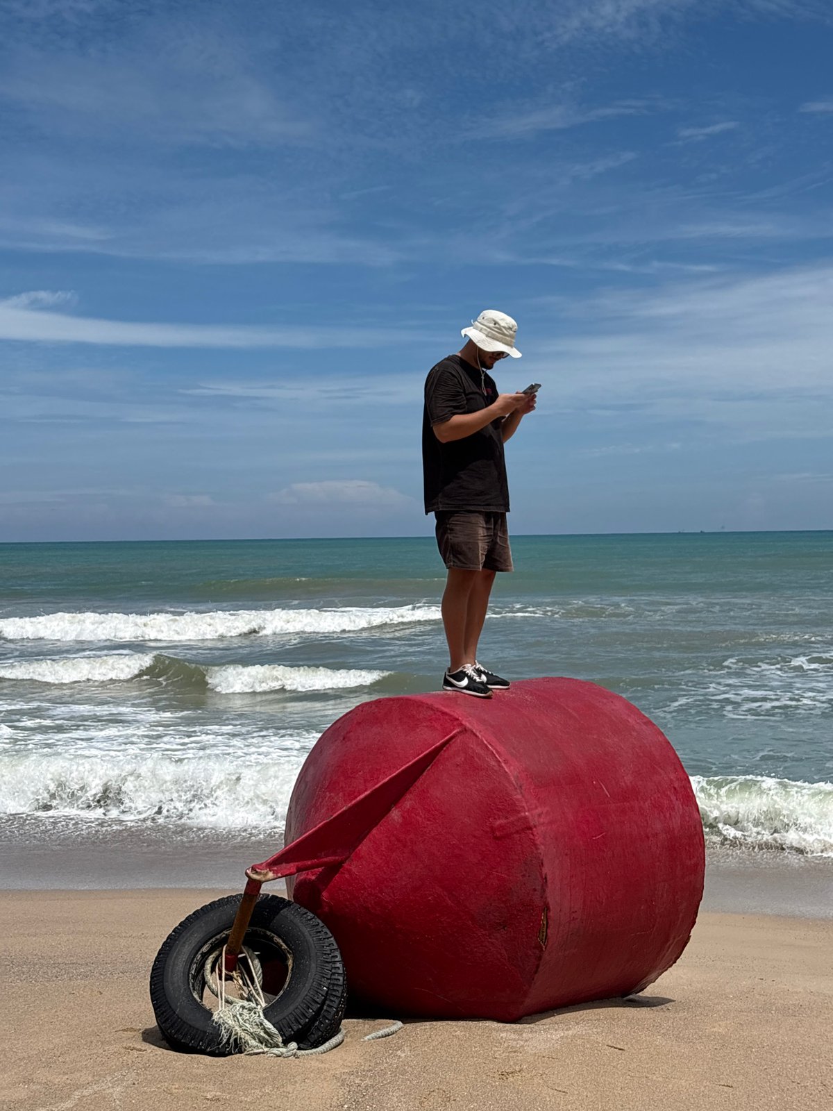 Man explores Choeng Thale beach at dawn, poses on red buoy