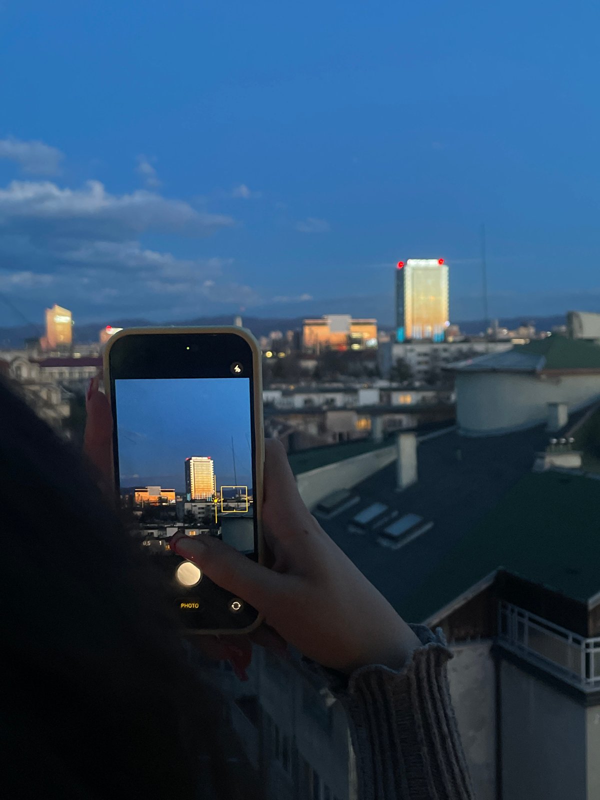 Tourist photographs Sofia skyline featuring East Plaza Hotel at dusk