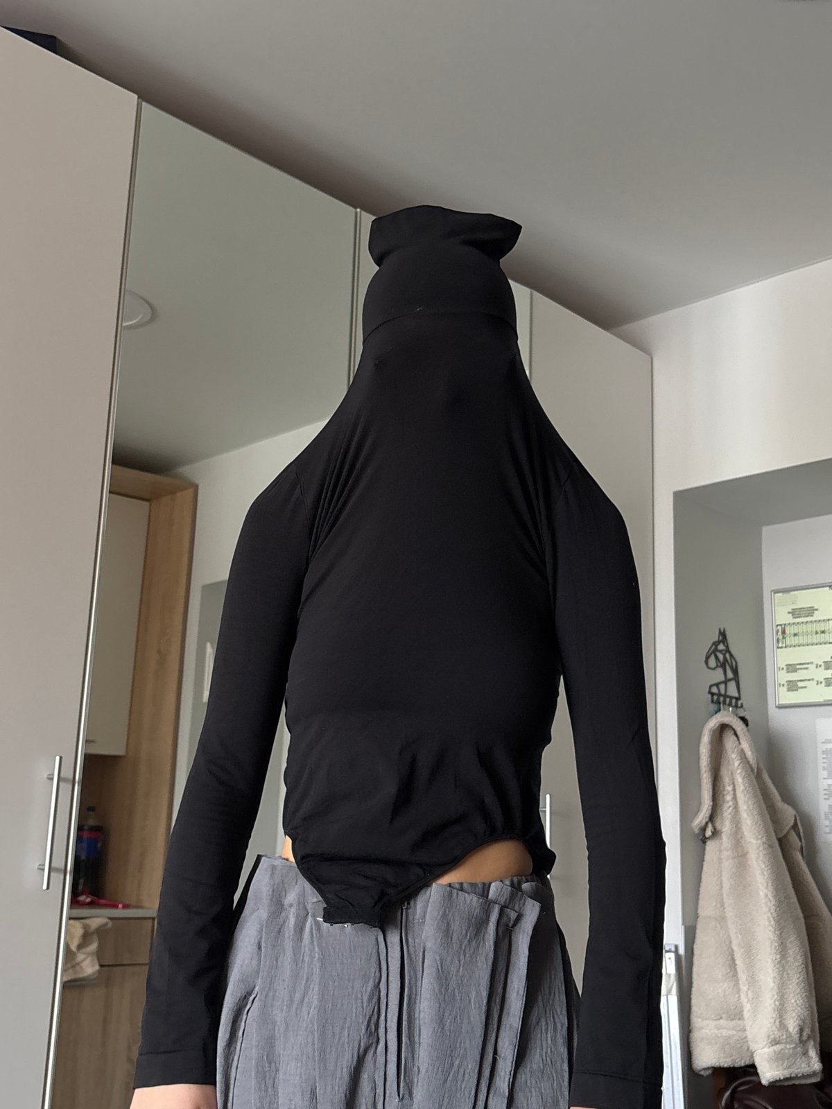 Person in black turtleneck observed at mirrored wardrobe