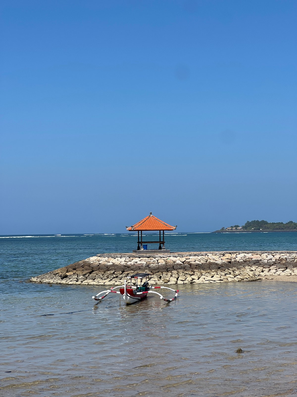 Sanur Beach on a sunny morning, boats, promenaders, and shrines