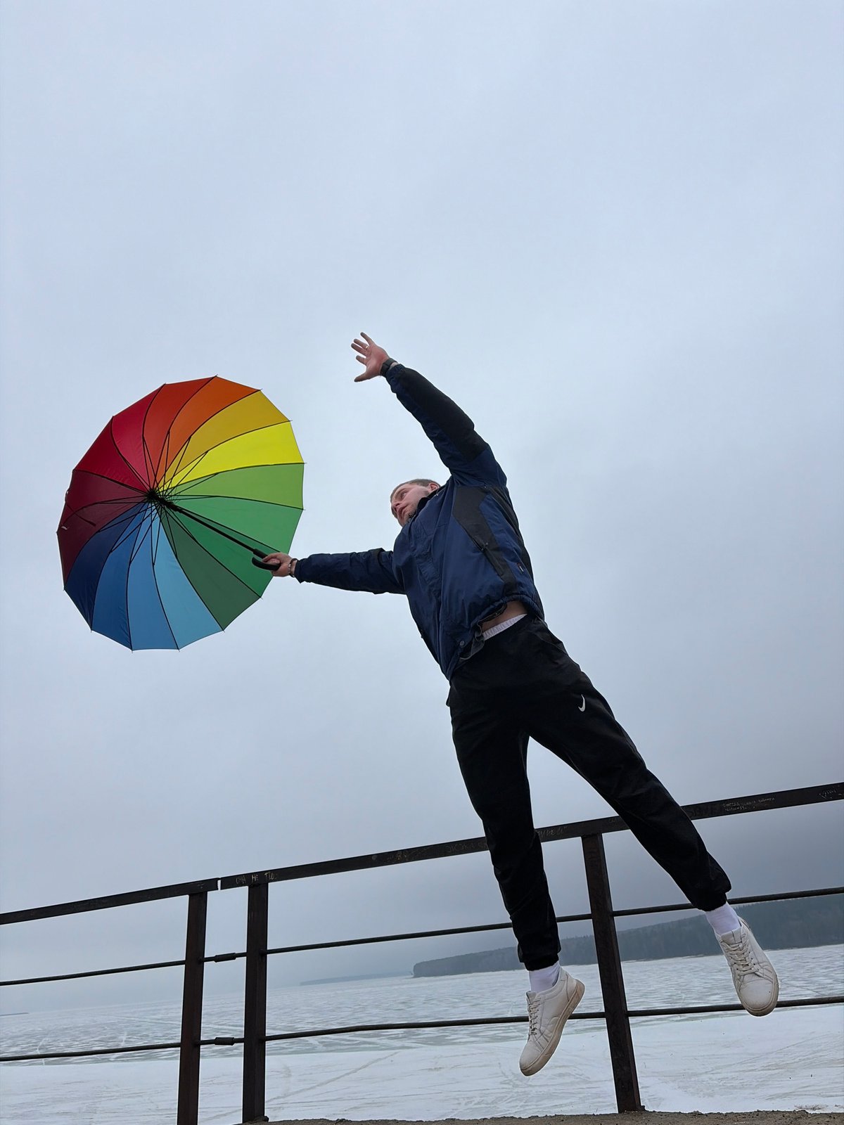 Person balances on moss-covered pipes with rainbow umbrella in Chaikovsky